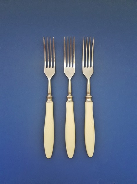 Three bone-handled forks on blue background. Declutter and simplify